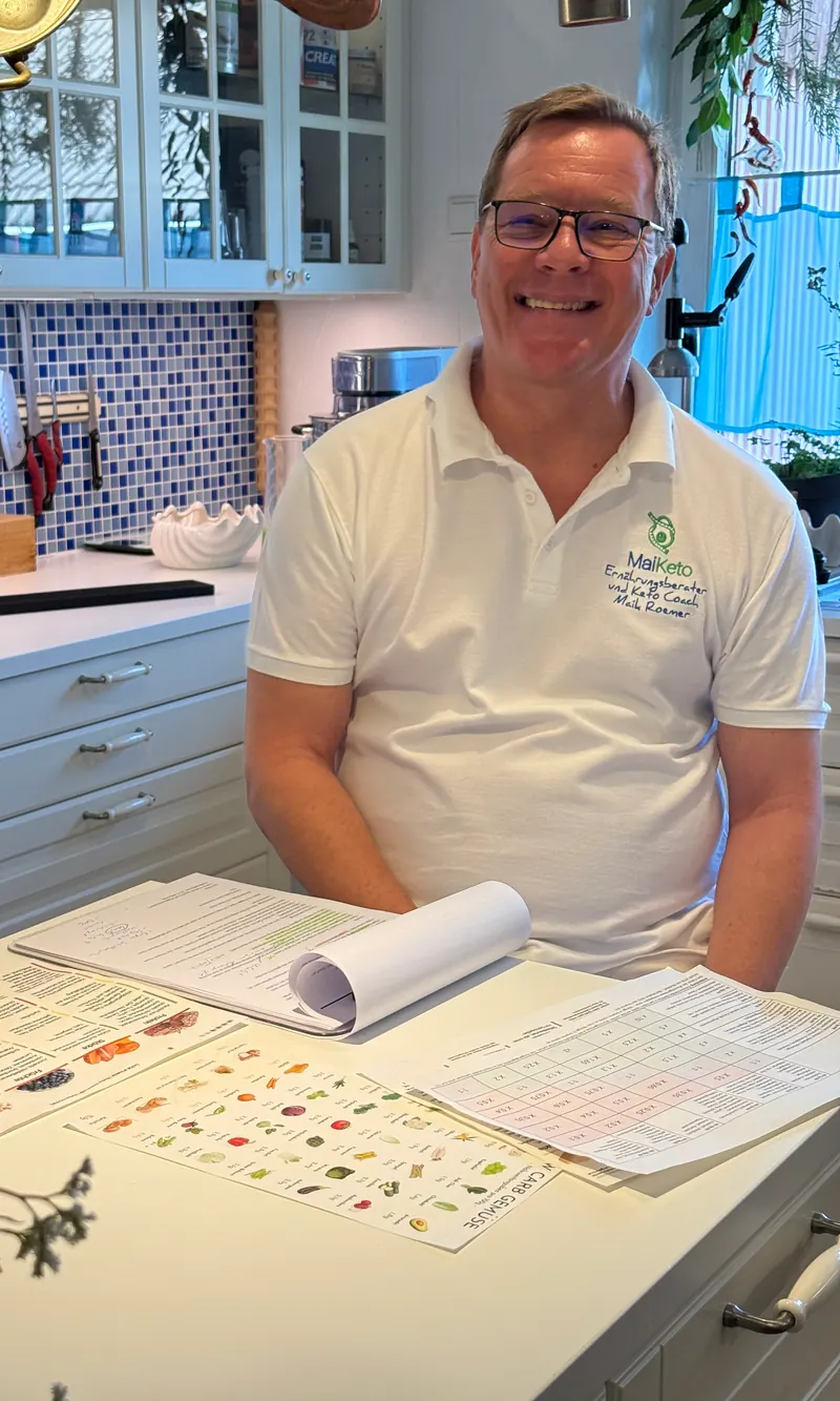 Maik Roemer lacht am Küchentisch über ausgedruckten Ernährungsplänen