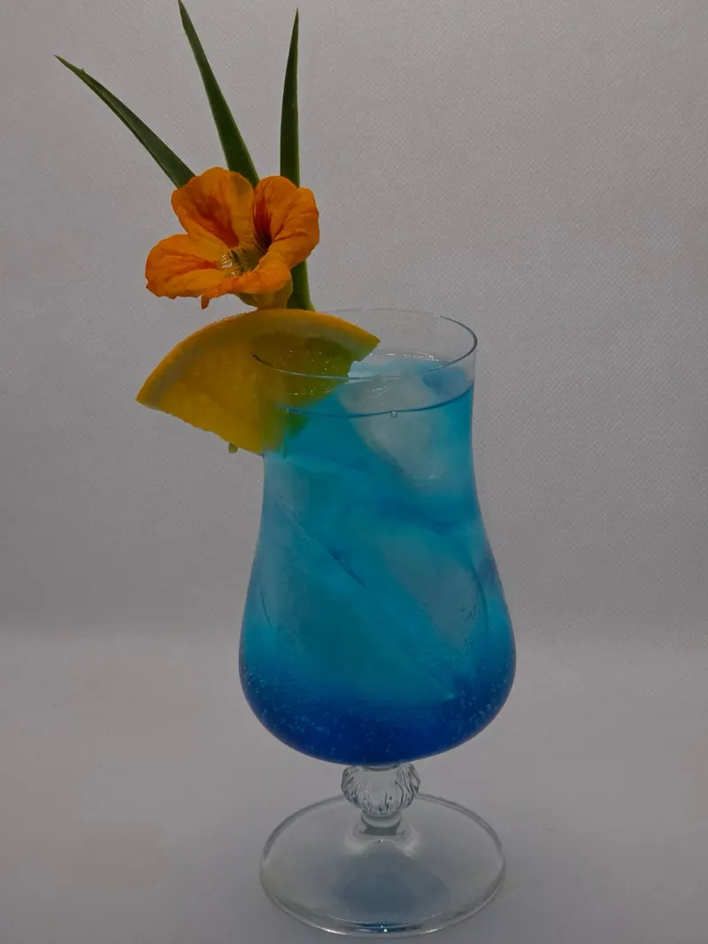 Blauer Cocktail im geschwungenen Glas mit Orangenscheibe und Kapuzinerkresse-Blüte