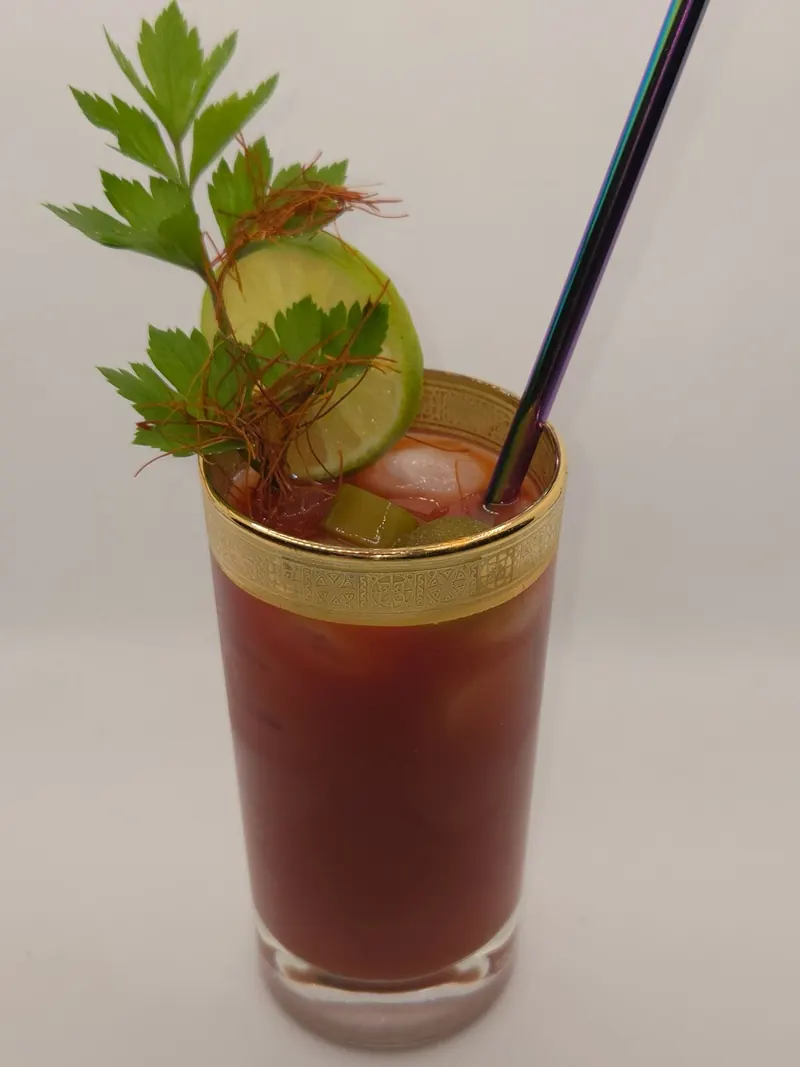 Roter Drink im Longdrinkglas mit Goldrand, garniert mit Liebstöckel und einer Limettenscheibe