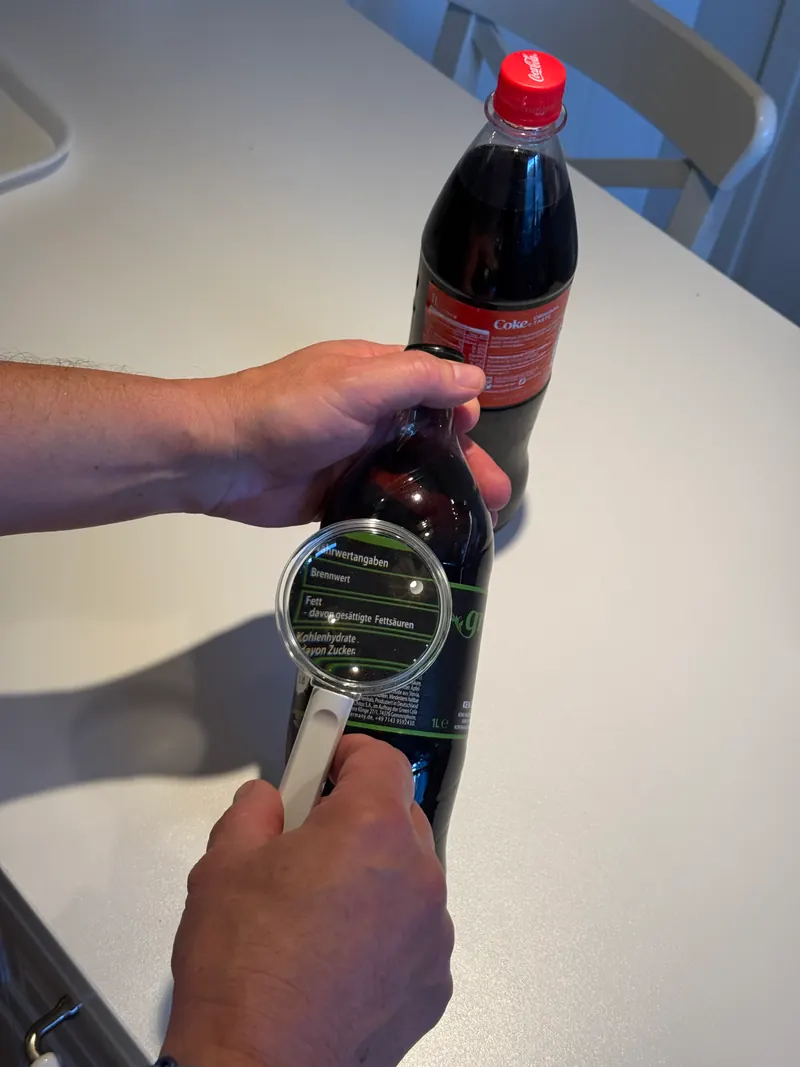 Mit der Lupe wird die Nährwerttabelle auf einer Flasche gelesen