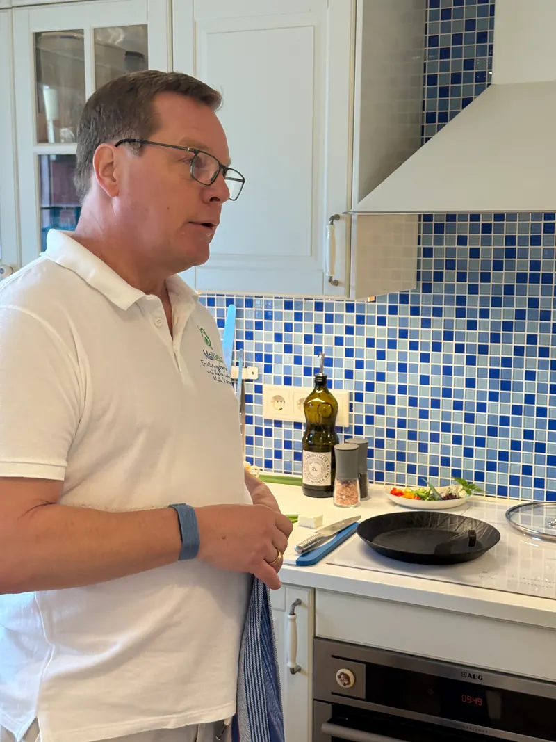Maik Roemer mit Küchentuch über der Schulter erklärt in seiner Küche