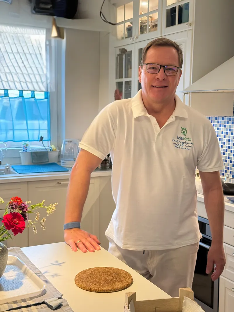 Maik Roemer steht an der Kücheninsel seiner Küche in Düsseldorf, daneben ein Blumenstrauß