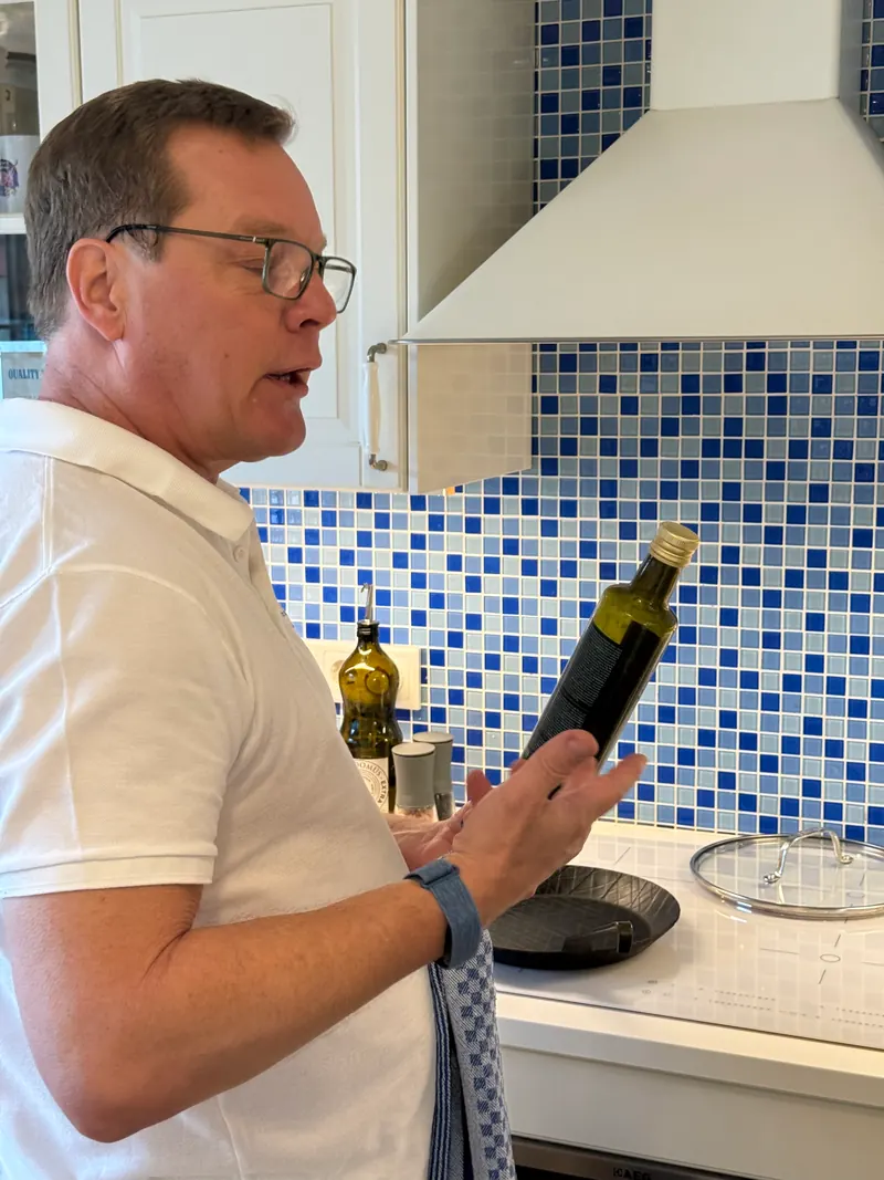 Maik Roemer erklärt beim Kochen eine Flasche Olivenöl