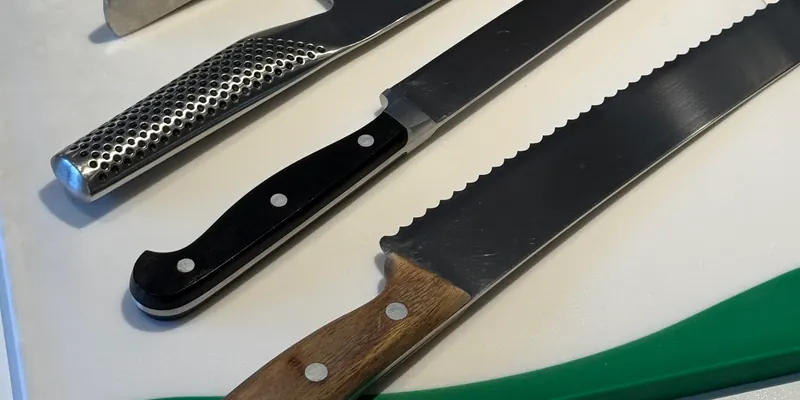Maiks Kochmesser nebeneinander auf dem Schneidebrett, Griffe aus Stahl, Kunststoff und Holz