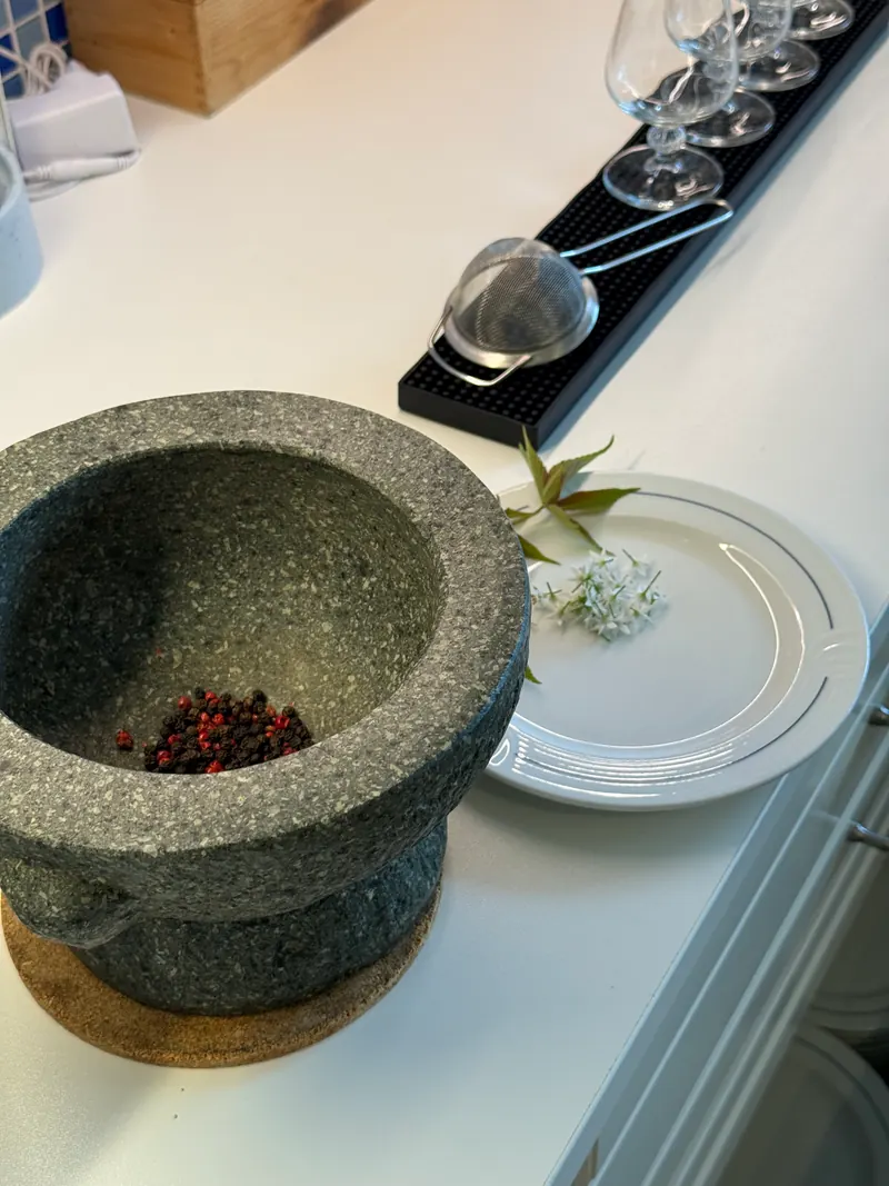 Steinmörser mit rosa Pfeffer neben Cocktailgläsern